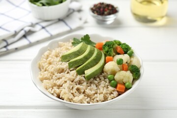 Tasty brown rice with vegetables in bowl on white wooden table, closeup