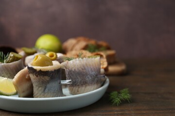 Delicious herring rolls with olives on wooden table, closeup. Space for text