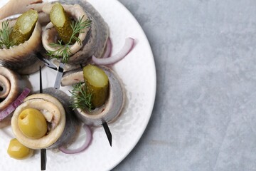 Delicious herring rolls with olives, pickles, dill and onion on gray textured table, top view....