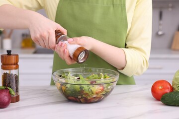 Woman salting tasty salad at white marble table in kitchen, closeup