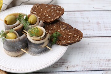 Delicious herring rolls with olives, dill and bread on white wooden table, closeup. Space for text
