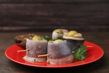 Delicious herring rolls with olives, parsley and bread on wooden table, closeup