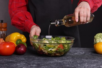 Woman pouring oil onto tasty salad at dark textured table, closeup