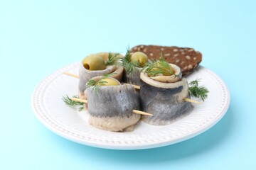 Delicious herring rolls with olives, dill and bread on light blue background, closeup