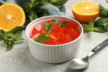Delicious jelly cubes in bowl, mint and orange on grey table, closeup