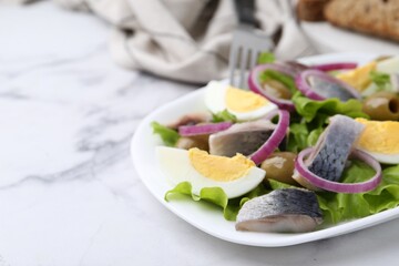 Delicious salad with herring, egg and vegetables on white marble table, closeup. Space for text