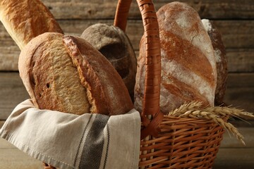 Different loaves of fresh bread and spikes in wicker basket on table, closeup