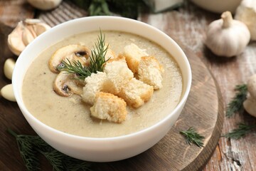 Delicious mushroom cream soup with croutons, dill and ingredients on wooden table, closeup