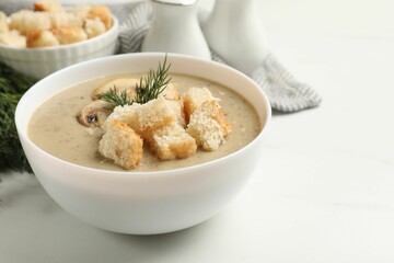 Delicious mushroom cream soup with croutons and dill served on white table, closeup