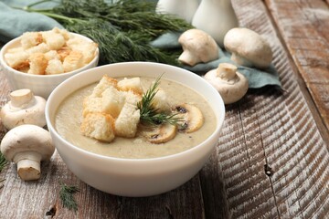 Delicious mushroom cream soup with croutons, dill and ingredients on wooden table