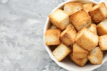 Tasty crispy croutons in bowl on grey textured table, top view. Space for text