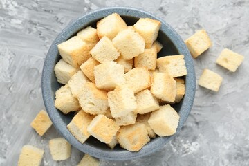Tasty crispy croutons in bowl on grey textured table, flat lay