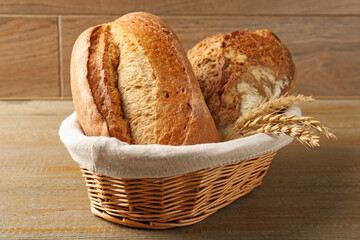 Different types of fresh bread and spikelets in wicker basket on wooden table, closeup