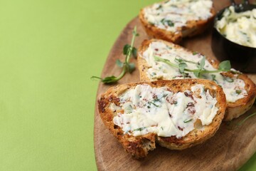 Tasty bread with garlic, herbs and oil on light green background, closeup. Space for text