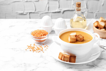 Delicious lentil cream soup served with croutons on white marble table