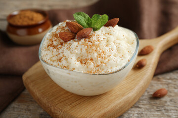 Delicious rice pudding with cinnamon, almonds and mint on wooden table, closeup