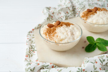Delicious rice pudding with cinnamon, almonds and mint on white wooden table, closeup. Space for text