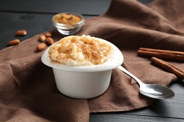 Delicious rice pudding with cinnamon in bowl, almonds and spoon on black wooden table, closeup