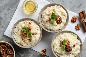 Delicious rice pudding with walnuts, cinnamon, mint and honey on grey table, flat lay