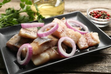 Pieces of herring with onions and parsley on wooden table, closeup