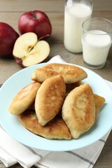 Delicious fried pyrizhky (stuffed pies) with apples and milk on wooden table, closeup