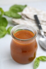 Tasty curry sauce in glass jar and basil on white tiled table, closeup