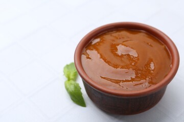 Tasty curry sauce and basil leaves on white tiled table, closeup. Space for text