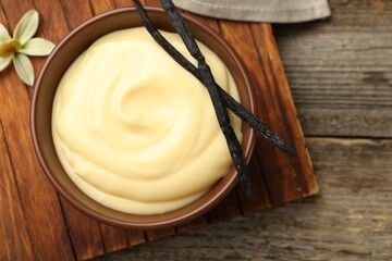Tasty vanilla pudding, pods and flower on wooden table, flat lay