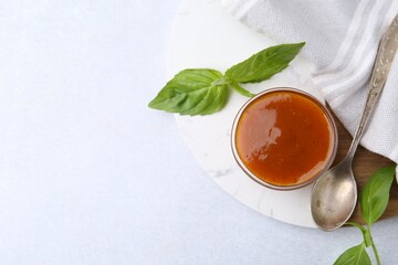 Tasty curry sauce in glass bowl and basil on white table, flat lay. Space for text