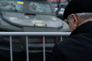 Elderly man observing military vehicle at public display in urban area during uncertain times of...