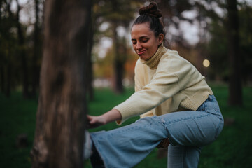 A young girl performs a stretching exercise in an outdoor park setting, wearing casual yet...
