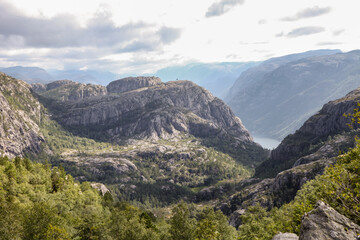 The mountains are covered in trees and rocks lysefjord, and the sky is cloudy