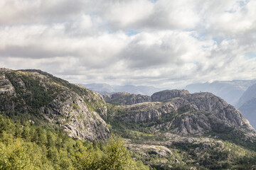 The mountains are covered in trees and rocks in Norway, and the sky is cloudy