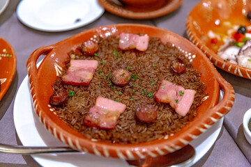 Arroz de Pato, Portuguese rice dish with smoked sausage and pork served in a decorative clay bowl,...