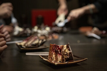 Celebration with Black Forest cake being sliced and served at a gathering, featuring layers of rich chocolate, cherries, and cream in a festive setting