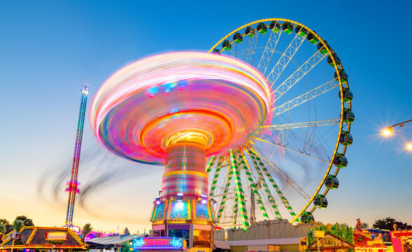 Ferris wheel, chain carousel and free-fall tower at the largest funfair in the Ruhr area. Evening atmosphere at the blue hour with colorful traces of light from rotating rides at the Cranger Kirmes