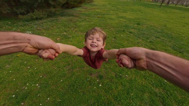 First-person view, father holding his son's hands, spinning him around in a circle at the park, joyful child laughs, enjoying the playful moment, creating happy childhood and family memories together