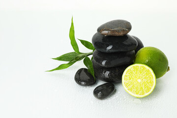 Spa composition with limes, massage stones and green leaves on wet surface, space for text