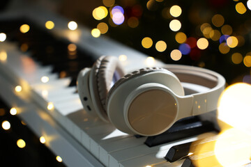 Headphones on electric piano against blurred lights, closeup. Bokeh effect