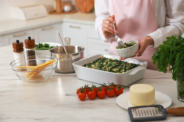 Woman making spinach lasagna at marble table in kitchen, closeup