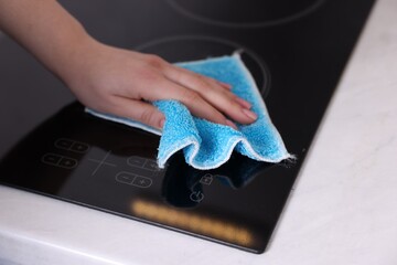 Woman cleaning induction cooktop with rag indoors, closeup