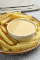 Tasty cheese sauce in bowl and French fries on grey table, closeup