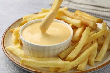Dipping French fry into cheese sauce at grey table, closeup