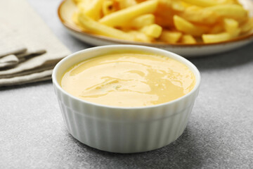 Tasty cheese sauce in bowl and French fries on grey table, closeup
