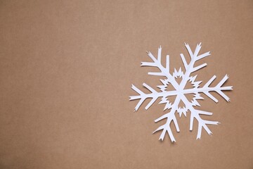 One paper snowflake on brown background, top view. Space for text