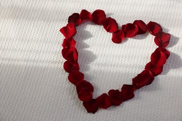 Obraz premium Heart made with beautiful rose petals on bed, top view. Space for text
