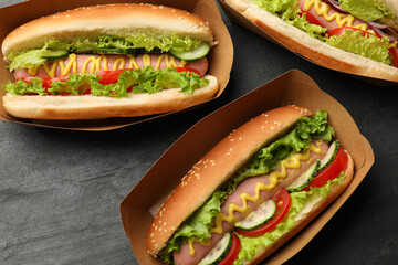 Tasty hot dogs with vegetables on black table, flat lay