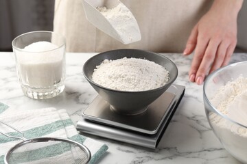 Woman putting sugar into bowl on digital kitchen scale at white marble table, closeup