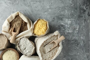Different types of flour in bags on grey textured table, flat lay. Space for text