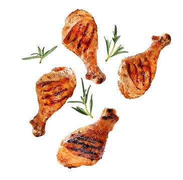 Grilled chicken legs or drumsticks falling down with herbs and colourful peppers isolated on white background. Juicy BBQ chicken drumsticks sprinkled with herbs and seasoning on white background..